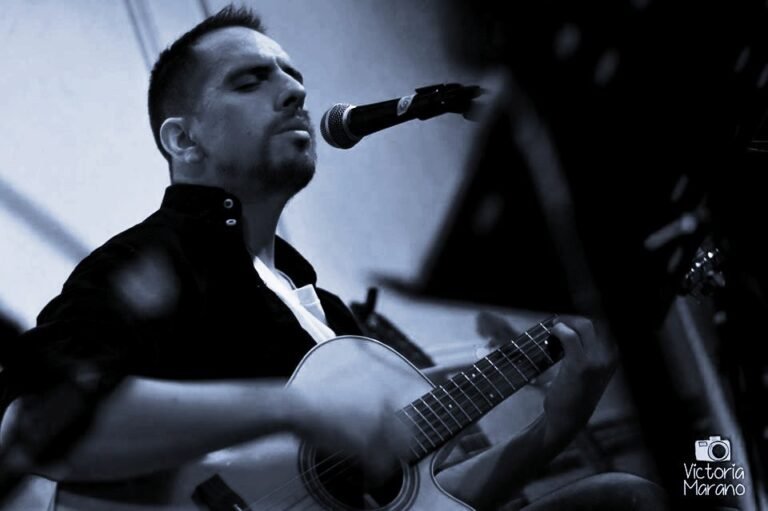 Martín Ponce cantando frente al micrófono con guitarra acústica, foto en blanco y negro